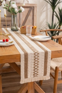 Detail of woven boho table runner with tassels and brown diamond pattern on a wood table