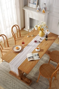 Detailed close-up of white crochet lace table runner with tassels on a wooden dining table