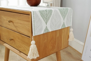 Detail of woven table runner with green leaf patterns and cream tassels on wood