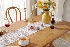 Detail of white lace table runner with hollow floral patterns on a wooden table