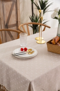 Detail of beige tablecloth featuring white daisy patterns and delicate fringe edges