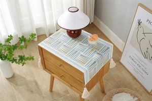 Close-up of geometric striped cover cloth with cream tassels on a wooden bedside table