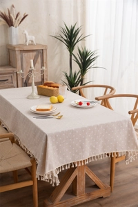 Detail of beige cotton-linen tablecloth with small daisy print and handmade fringe edge