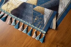 Close-up of luxury table runner featuring gold geometric jacquard and delicate blue tassels