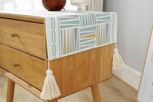 Close-up of geometric jacquard dust cover with tassel details on a wooden bedside table
