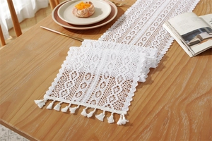 Close-up of white crochet lace table runner with hollow floral pattern and elegant tassels