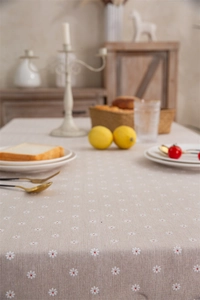 Close-up of linen tablecloth with white daisy floral prints and elegant tassel edges
