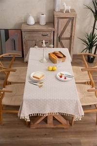Close-up of beige daisy pattern tablecloth with elegant tassel trim in a rustic setting