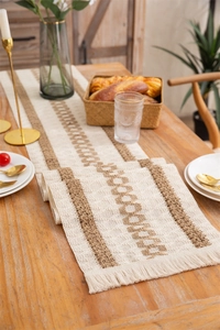 Detail of woven table runner with geometric textures and fringe tassels on a wooden table