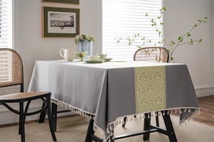 Detail of grey jacquard tablecloth with yellow retro scroll pattern and white tassel edges