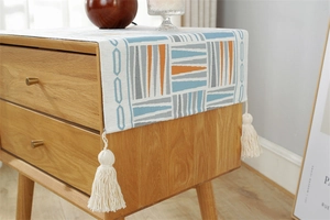 Close-up of woven fabric dust cover with geometric stripes and white tassels on wood