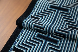 Macro shot of geometric embroidered chenille table runner with blue maze patterns