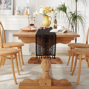 Black lace table runner with hollow geometric patterns and elegant tassels on a wooden table