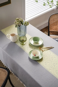 Detail of dark grey textured tablecloth with vintage yellow runner and white tassel fringe