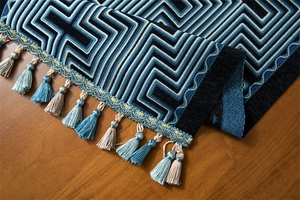 Detailed view of geometric jacquard table runner with blue maze patterns and tassels