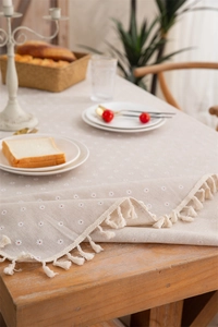 Detailed close-up of beige daisy print tablecloth with elegant white fringe tassels