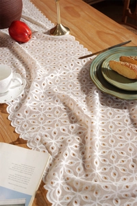 Macro detail of white scalloped lace table runner with floral embroidery on wooden table