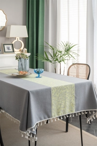 Detail of grey tablecloth featuring jacquard leaf patterns and elegant cream fringe tassels
