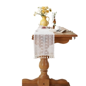 White crochet lace table runner with floral hollow patterns and tassel fringe on wooden table