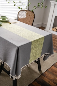 Detail of grey jacquard tablecloth featuring geometric patterns and cream tassels