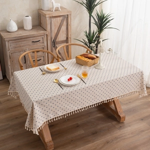 Beige cotton linen tablecloth with blue dot prints and tassel fringe on a wooden table