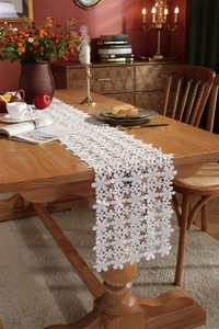 Close-up of white floral hollow lace table runner draped on a dark wooden table surface