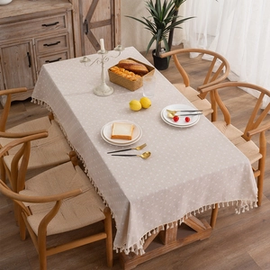 Modern beige daisy floral tablecloth with tassel edges on a wooden dining table