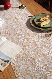 Close-up of white rose lace table runner with wavy edges on a wooden dining table
