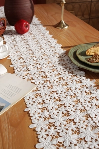 Macro shot of white lace table runner with hollow floral pattern on a wooden dining table