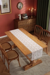 Close-up of white lace table runner with intricate rose patterns on a wooden dining table