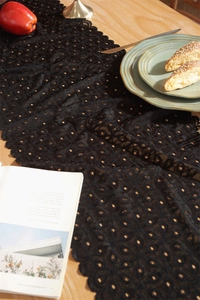 Detail shot of black hollow floral lace table runner with scalloped edges on wood