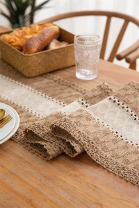 Detail of hand-woven jute table runner with white lace stitching on a wooden dining table