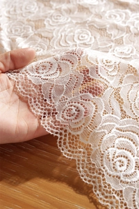 Macro shot of white floral lace fabric with elegant rose patterns and scalloped edges