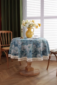 Detail of blue daisy jacquard tablecloth with white woven tassels on a wooden round table