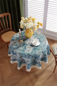 Detailed view of round jacquard tablecloth with blue daisies and beige fringe edges