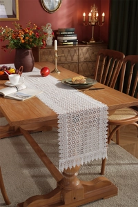 Macro detail of intricate white lace table runner with floral cutout patterns and fringe