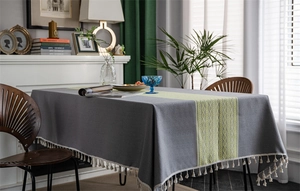 Detail of grey jacquard tablecloth featuring green geometric patterns and white tassels