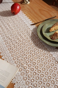 Detailed view of white hollow lace table runner with floral crochet patterns on wooden table