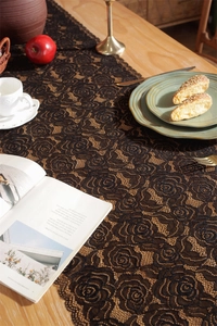 Close-up of black lace table runner with intricate rose patterns on a wooden dining table