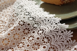 Close-up of white hollow embroidered lace table runner with floral patterns on wood