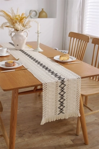 Détail d'un chemin de table tissé montrant des motifs géométriques et des pompons fins
