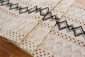 Détail d'un chemin de table en coton et lin tissé avec motifs géométriques et pompons