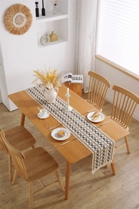 Détail d'un chemin de table tissé avec motif en losange et pompons sur table en bois