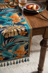 Détail d'un chemin de table en jacquard tropical avec motifs feuilles et glands colorés