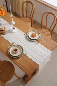 Close-up of white jacquard table runner with bohemian tassels on a rustic wooden dining table