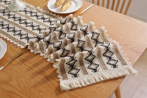 Détail d'un chemin de table tissé avec glands et motifs géométriques en losange sur bois