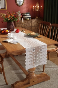Detailaufnahme weißer Tischläufer aus Spitze mit Blumenstickerei auf dunklem Holztisch