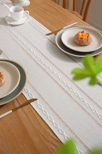 Close-up of beige jacquard table runner with braided embroidery and fringe on wood