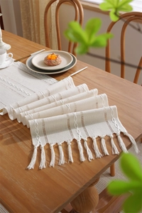 Detail of cream polyester jacquard table runner with textured knit and tassel edges
