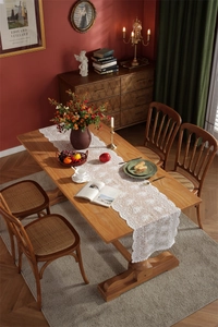 Detail eines weißen Spitzen-Tischläufers mit Blumenstickerei auf dunklem Holztisch